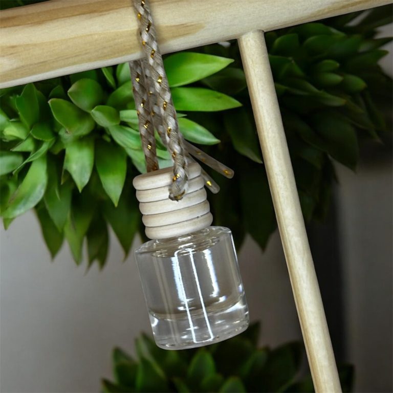 Flacon transparent suspendu avec un cordon en métal, près d'une plante verte.