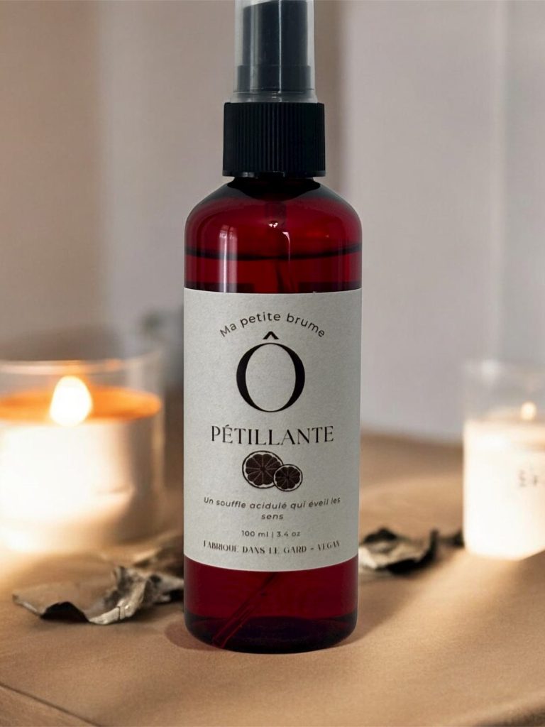 Flacon de spray brillant, étiqueté, posé sur une surface avec des bougies éclairées.